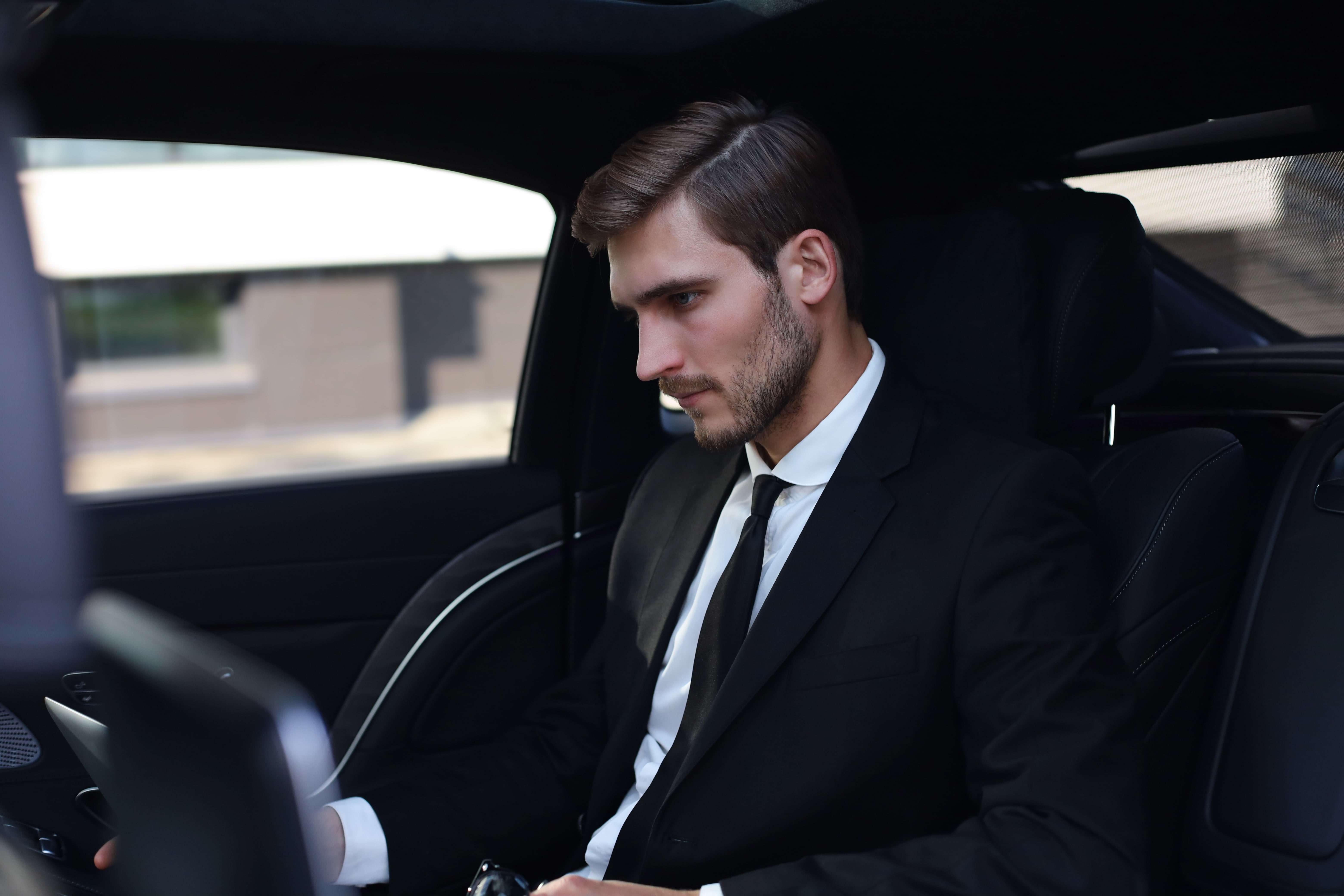 handsome-confident-businessman-suit-talking-smart-phone-working-using-laptop-while-sitting-car-min